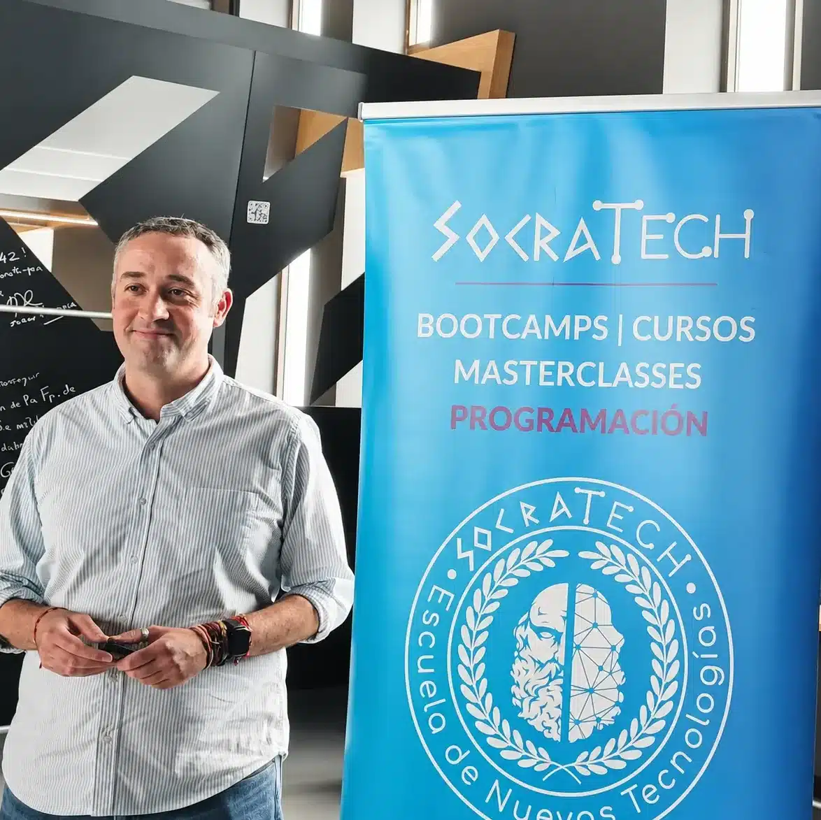 Carlos junto con un banner con el logo de SocraTech